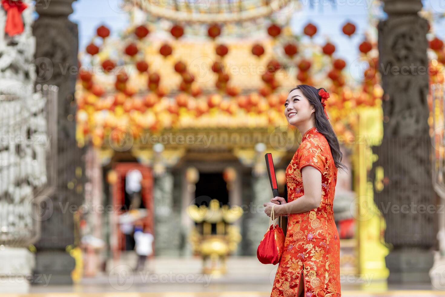Asian woman in the red cheongsam qipao dress holding paper fan while visiting the Chinese Buddhist temple during lunar new year for traditional culture photo