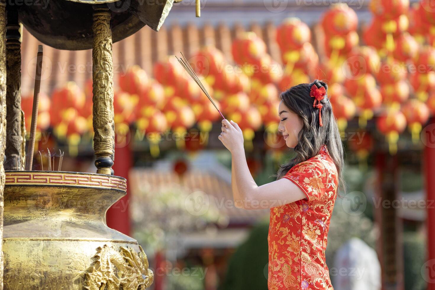 Asian woman in red cheongsam qipao dress is offering incense to the ancestral god inside Chinese Buddhist temple during lunar new year for for best wish blessing and good luck photo