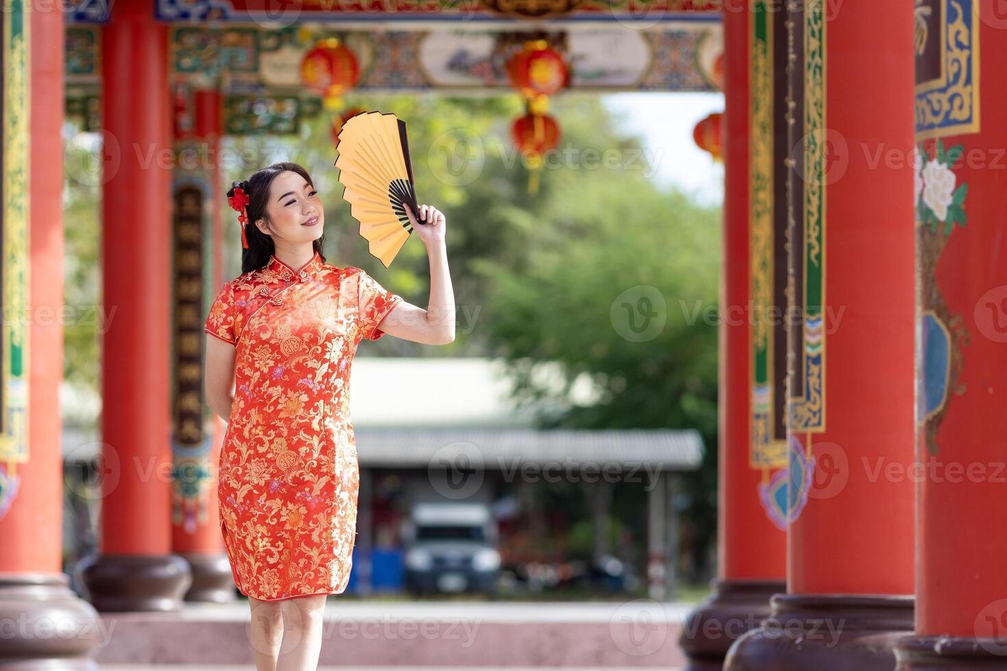 Chinese woman in red cheongsam qipao dress holding paper fan while visiting the Chinese Buddhist temple during lunar new year for traditional culture photo