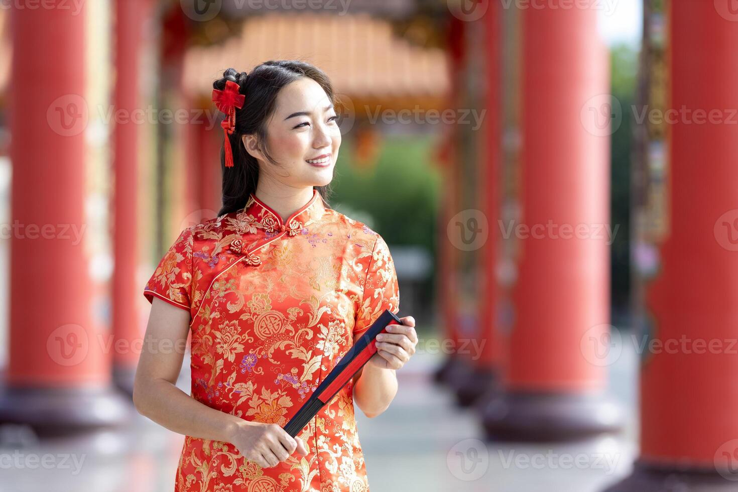 Asian woman in red cheongsam qipao dress holding paper fan while visiting the Chinese temple during lunar new year for traditional culture photo