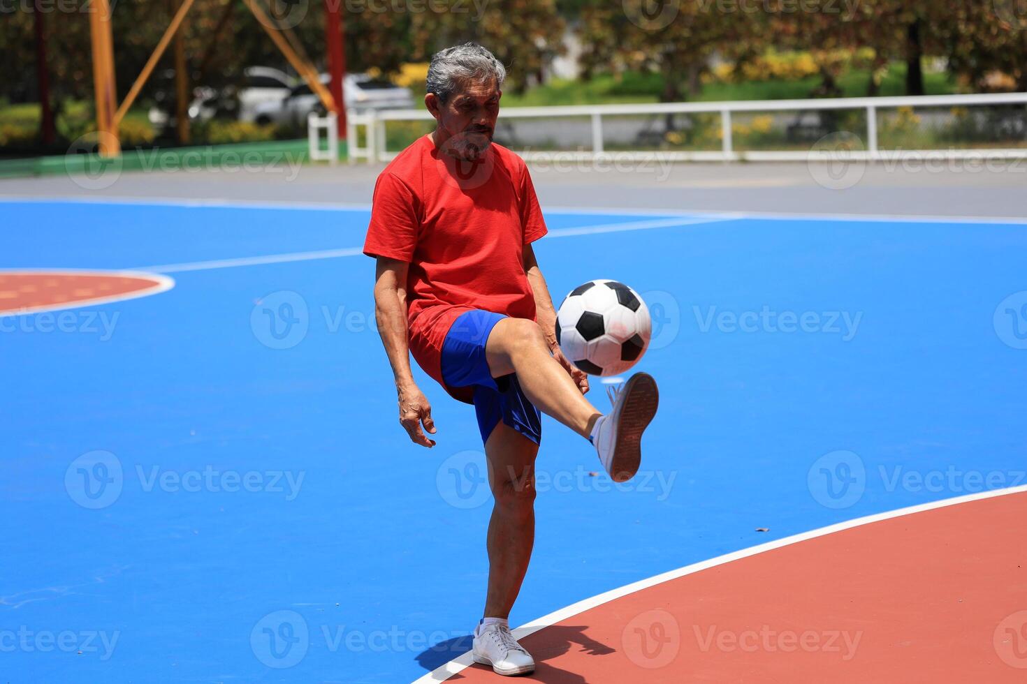 Senior Asian man in retirement age playing soccer football handling at outdoor court for healthy and fun activity to exercise and workout against aging illness photo
