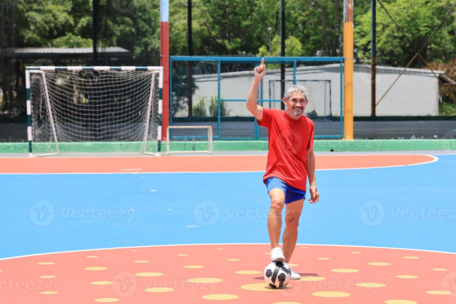 Senior Asian man in retirement age playing soccer football at outdoor court for healthy and fun activity to exercise and workout against aging illness photo