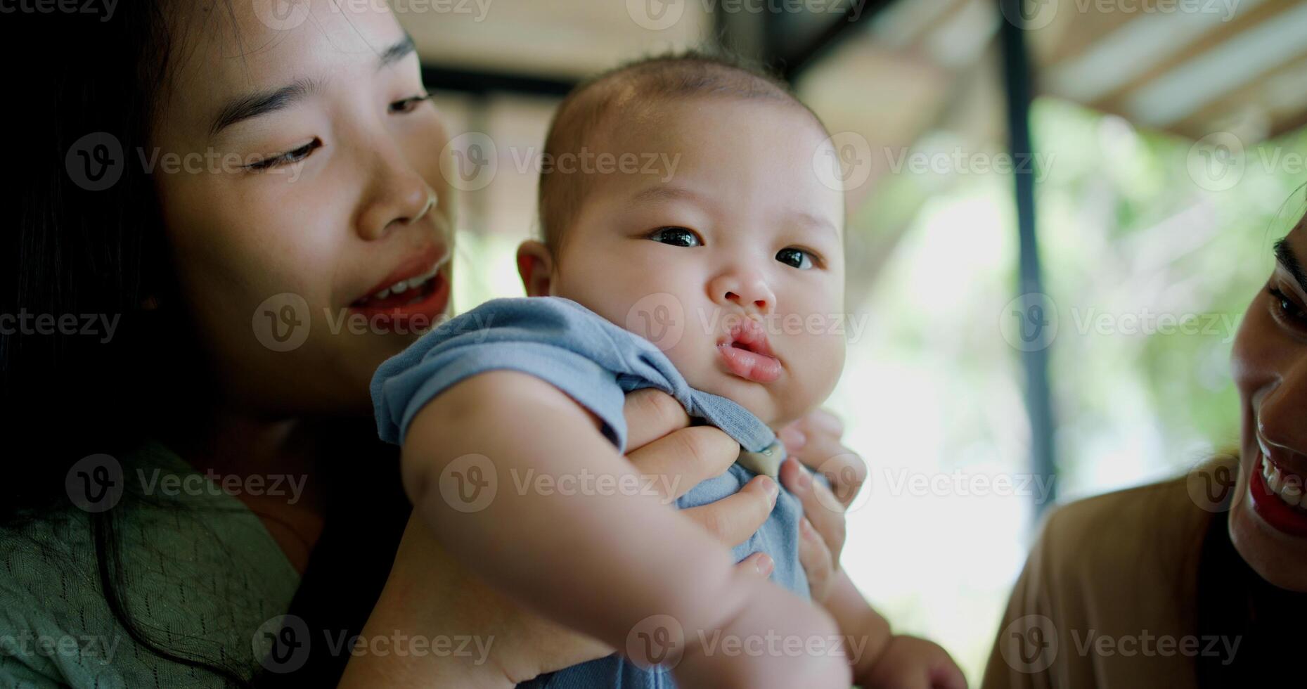 Selective focus, Happy moment in a coffee shop as two women smile and play with a baby boy. Family enjoying time together. photo