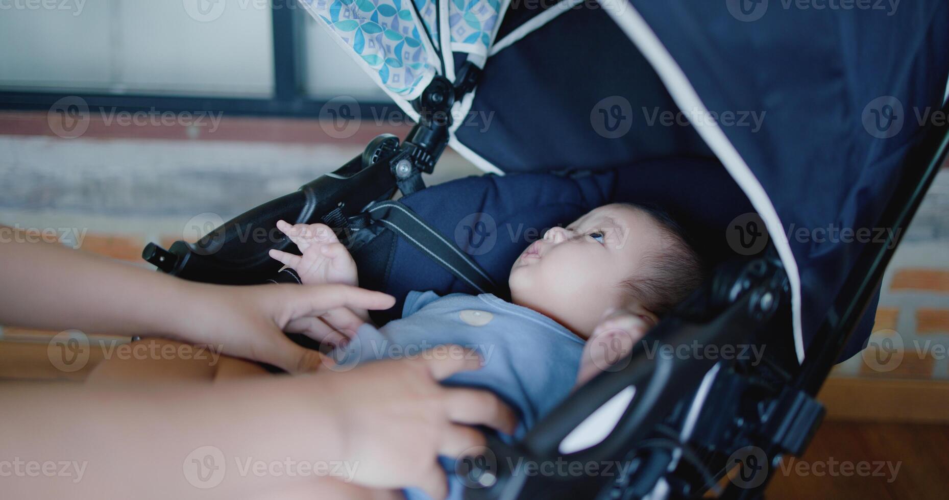 Selective focus, Hand of Young mother happily playing with little boy lying in baby stroller in a cafe. Family enjoying happy time together. Happy lifestyle. photo