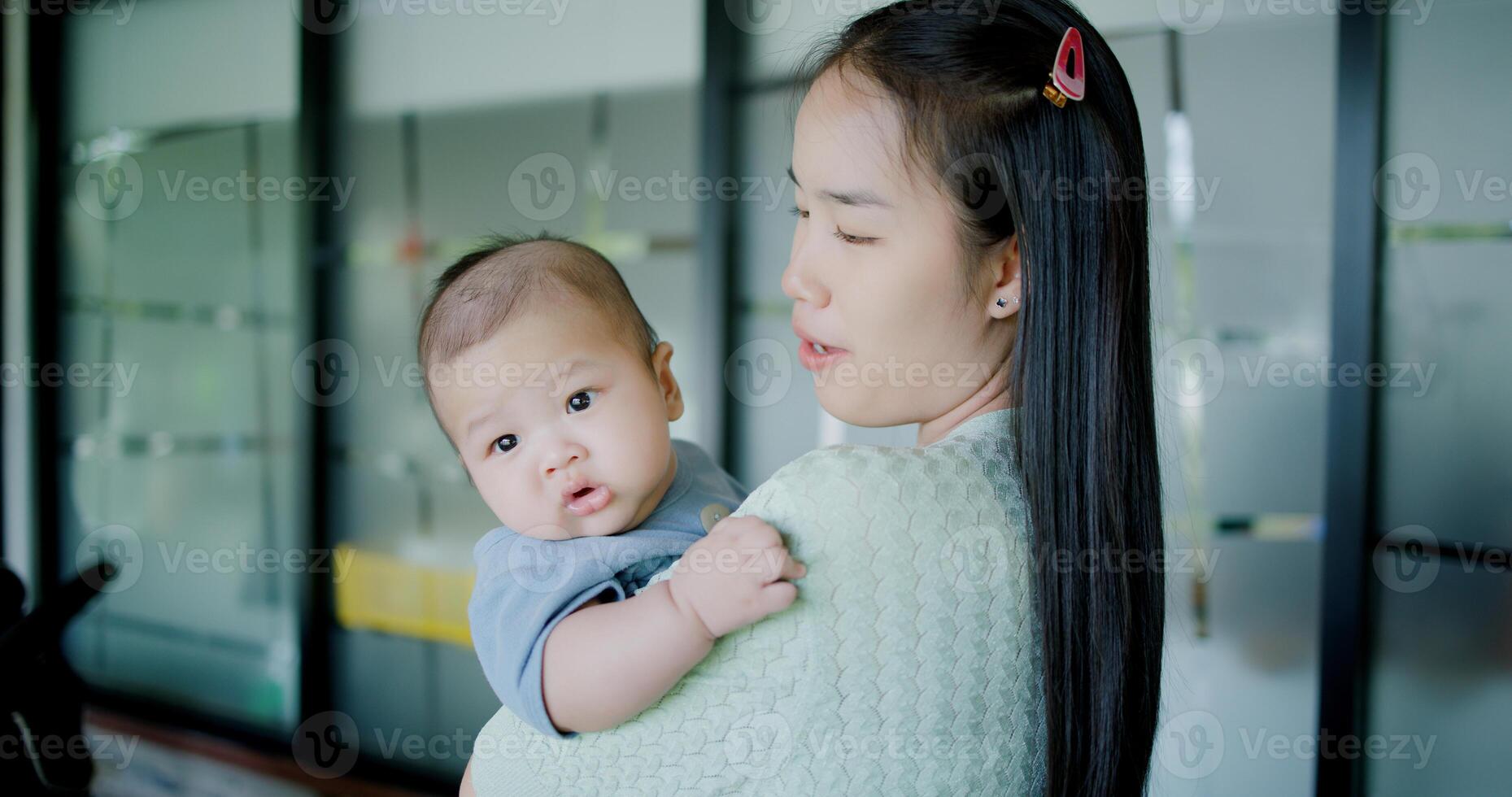 Portrait of Beautiful woman stands in a coffee shop, smiling warmly as she gently cradles a baby boy in her arms. Relaxed atmosphere add to the heartwarming moment. photo