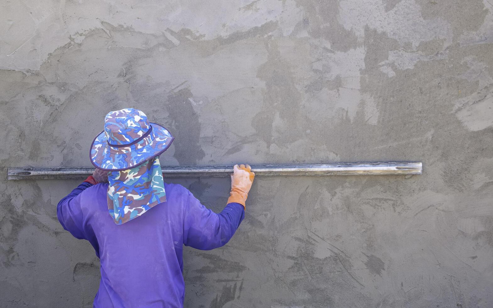 Rear view of Asian builder worker using long trowel to plastering cement on concrete wall background in house construction site photo