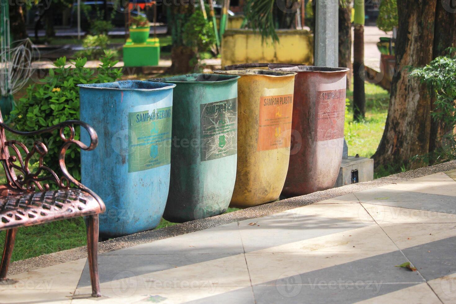 A row of colorful trash bins for waste segregation in an outdoor park setting, promoting eco-friendly practices photo