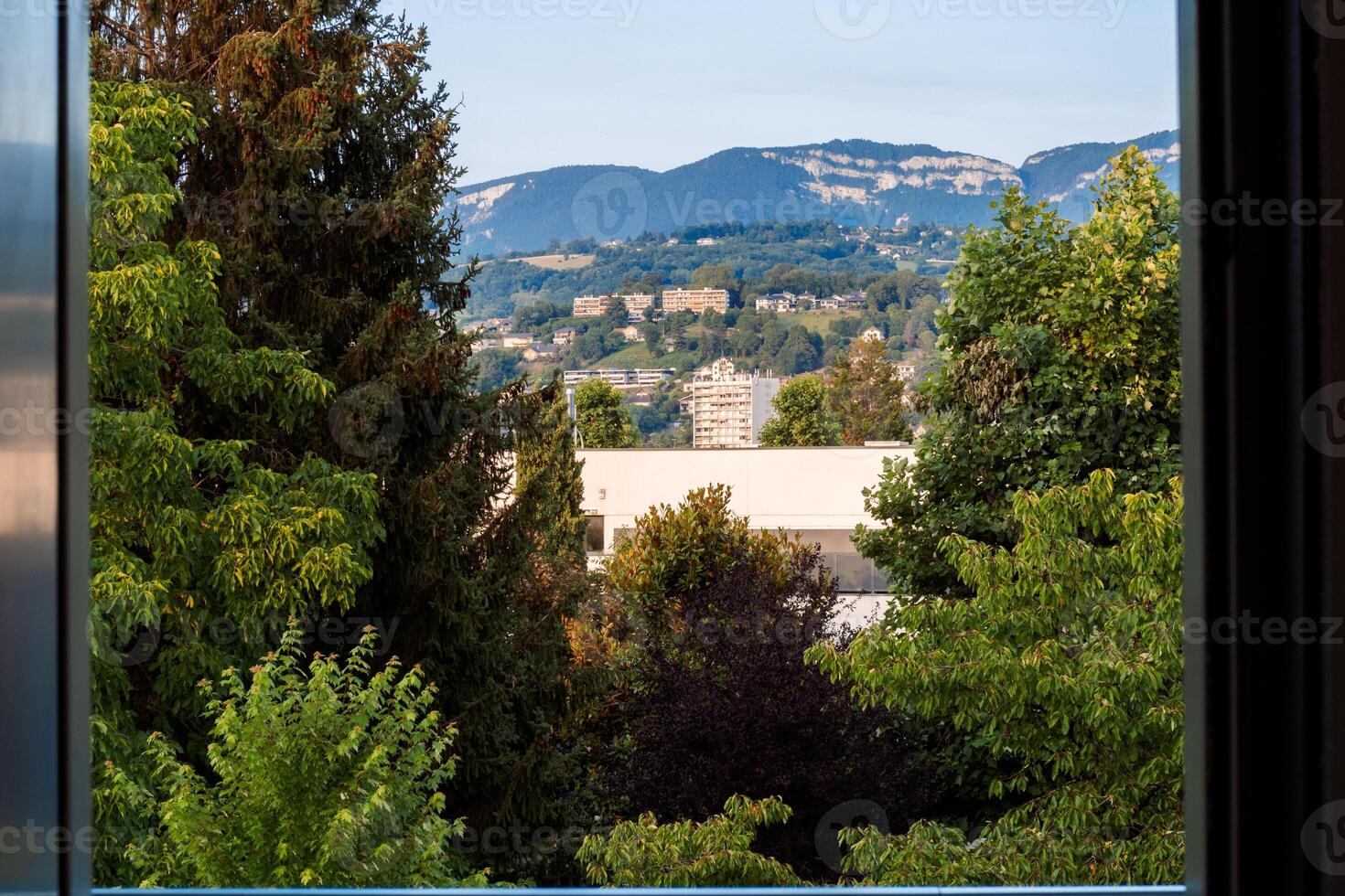Urban buildings and green trees viewed through a window frame with a mountain range in the background photo