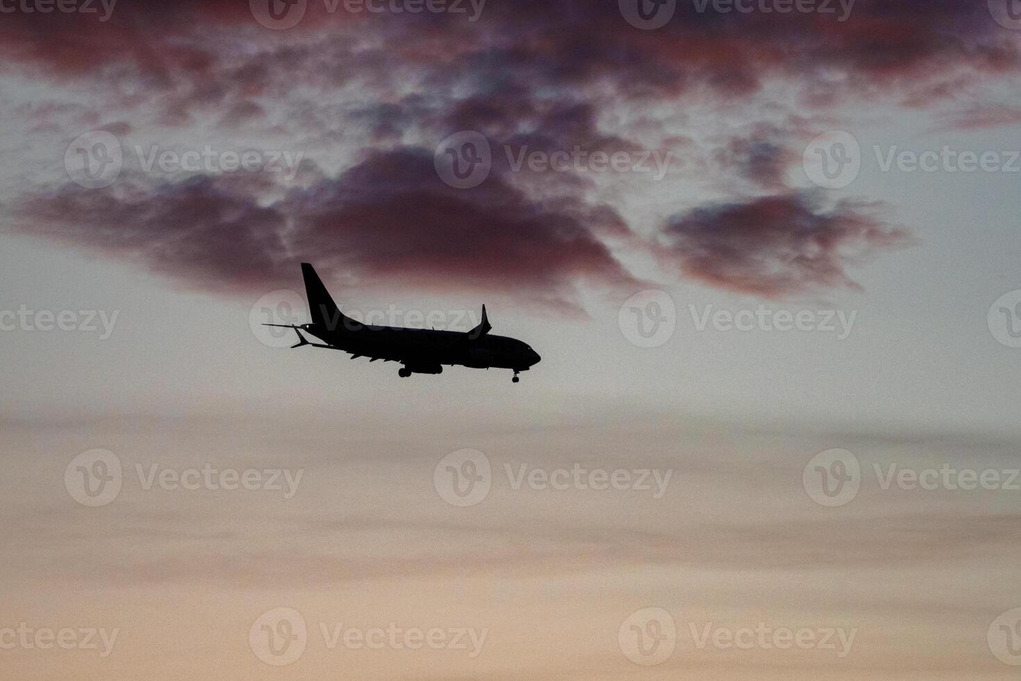 Silhouette of a commercial airplane flying against a vibrant dusk sky with shades of purple, pink, and blue, highlighting the aircraft's shape in the atmospheric sunset light photo