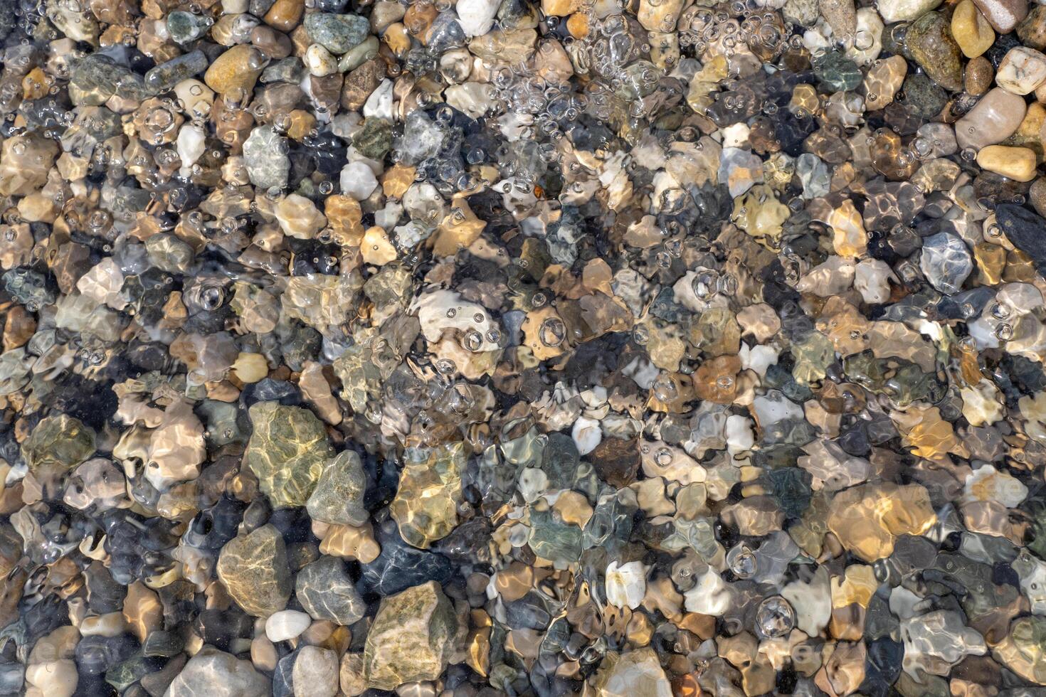 Natural pebbles of various colors and sizes submerged underwater with visible ripples and light reflections photo