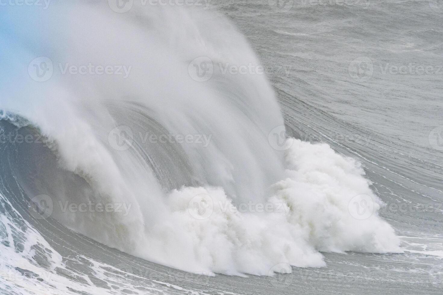 Powerful wave with ocean spray crashing near the coastline at Nazare in Portugal photo