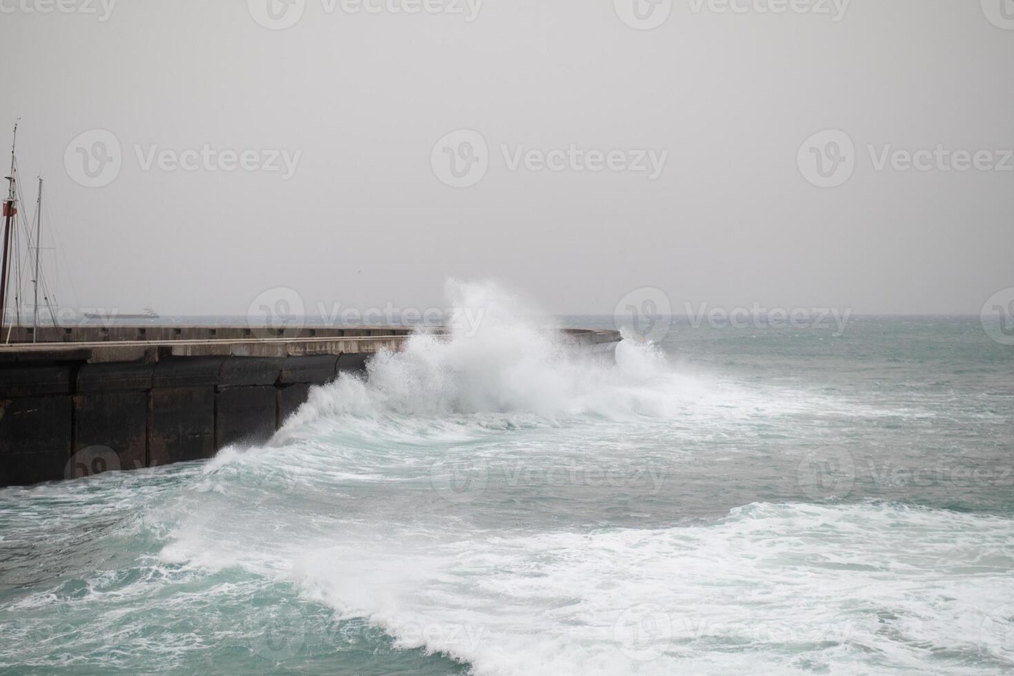 Rough ocean waves crashing powerfully against a concrete pier on a foggy day, with water spraying over the edge and creating a dramatic scene photo