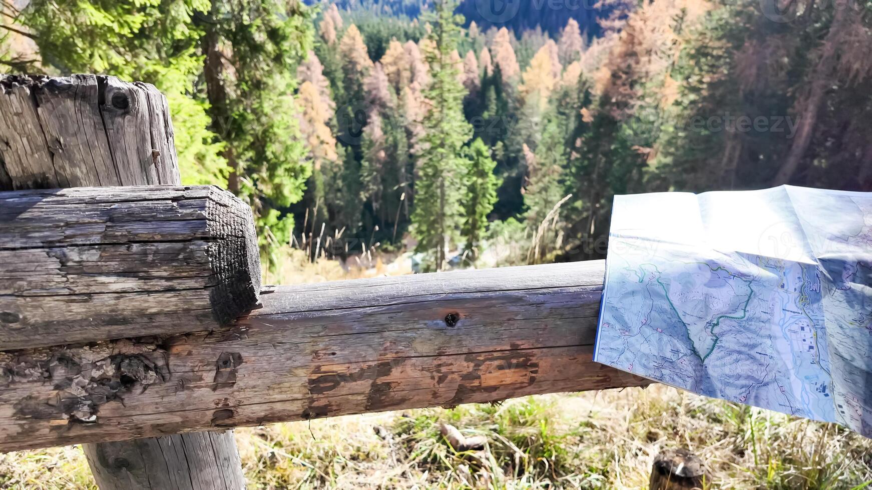 A detailed hiking map rests on a rustic wooden fence in a sunlit forest, capturing the essence of autumn exploration photo