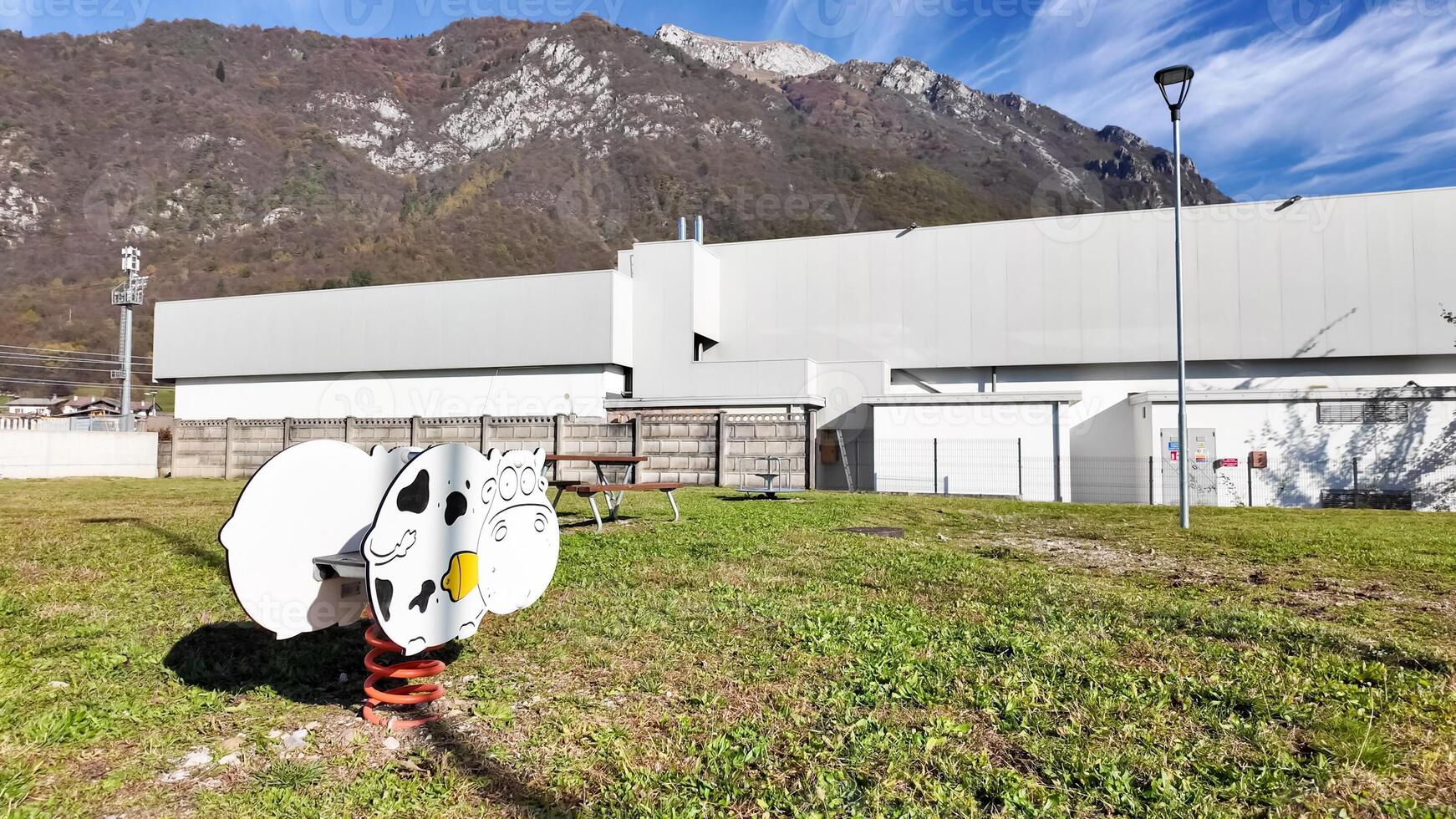A sunny day in an empty playground with a cow themed spring rider near an industrial building, highlighting urban solitude photo