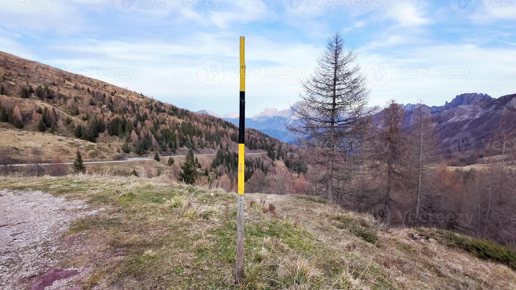 A solitary yellow and black pole stands in an autumnal mountain landscape, symbolizing solitude and the winter season in the Dolomites photo