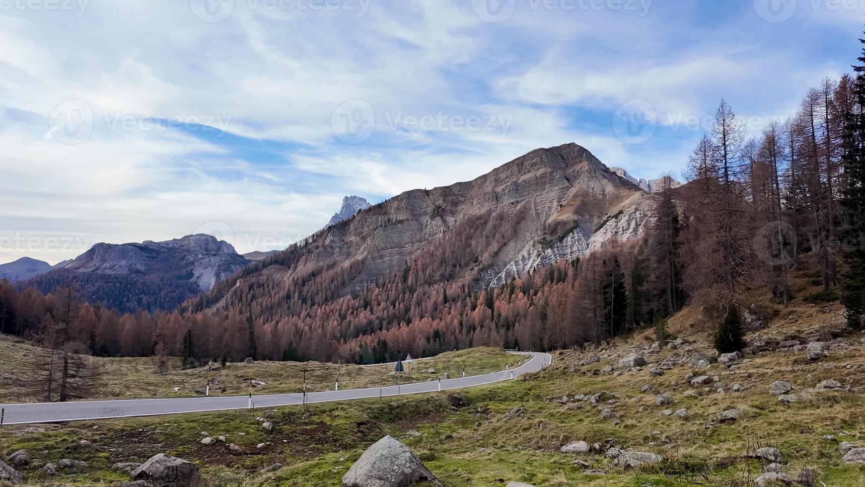 Scenic mountain landscape with winding road and autumnal forest under a partly cloudy sky, ideal for nature tourism or travel themed content photo