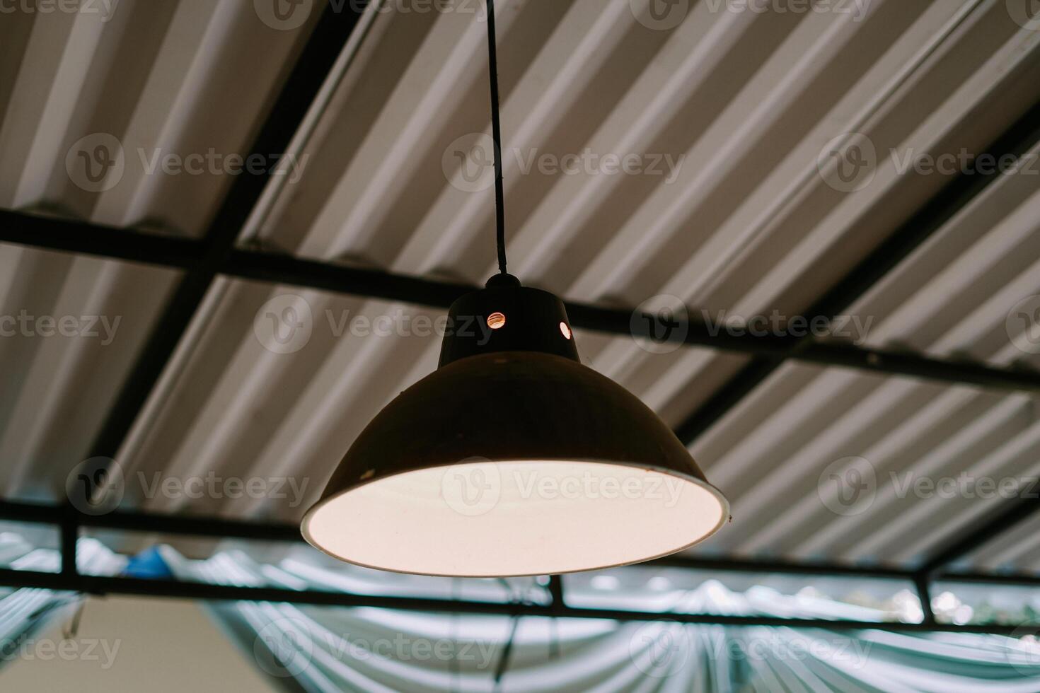 Black industrial pendant light hanging from a corrugated metal ceiling. photo
