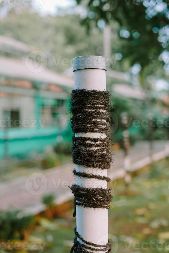 White pole with black rope wrap, blurred green background, outdoor setting. photo