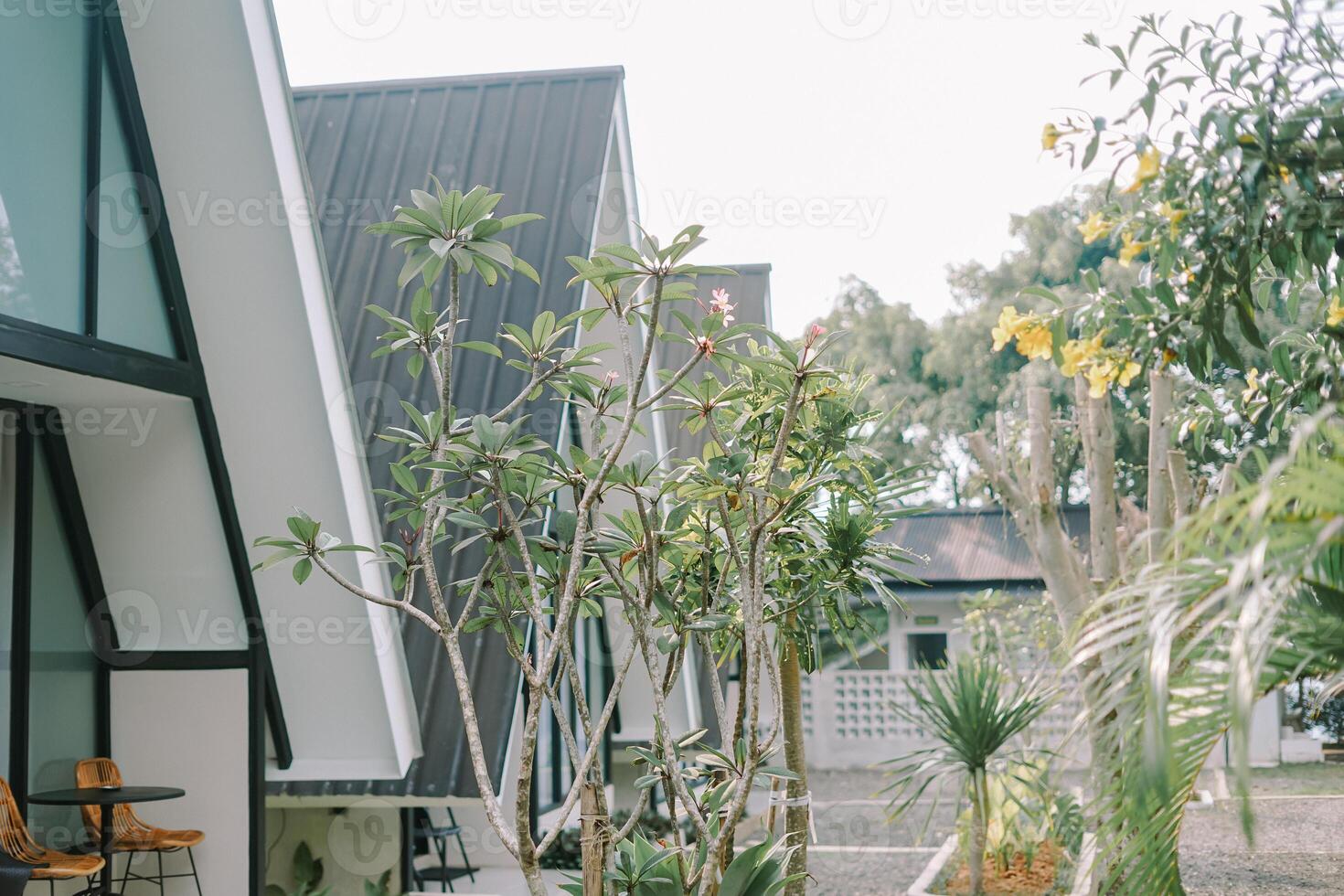 Modern A-frame cabin with large windows and a wicker chair in a cozy outdoor setting. photo