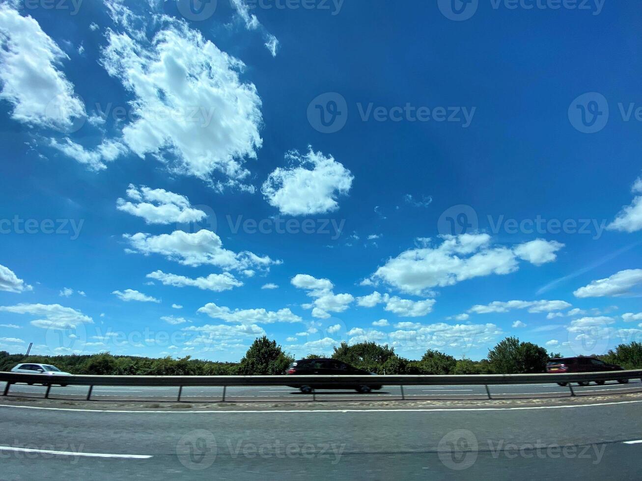 A car driving on a highway with blue skies and clouds photo