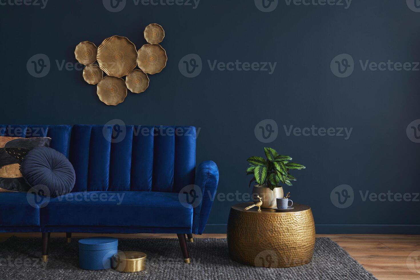 Elegant modern living room interior design with glamour blue velvet sofa, pouf, golden metal side table, plants and modern home accessories. Dark blue wall. Template. Copy space. photo