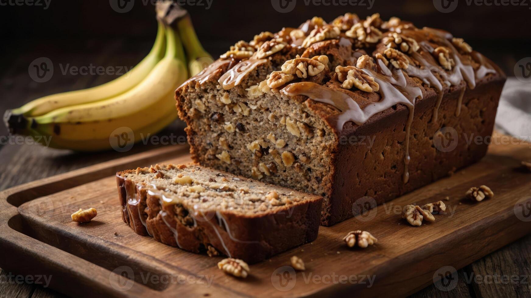 A loaf of banana bread topped with nuts and glaze, sliced on a wooden board with bananas. photo