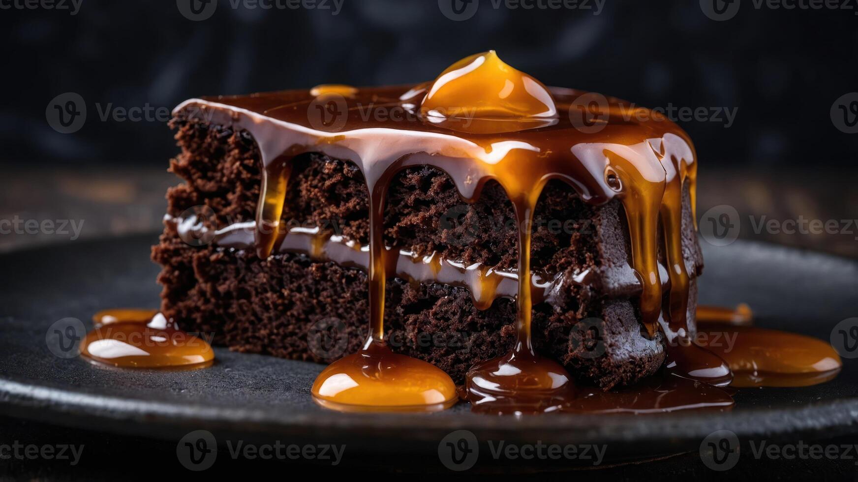 A decadent chocolate cake slice drizzled with caramel sauce on a dark plate. photo