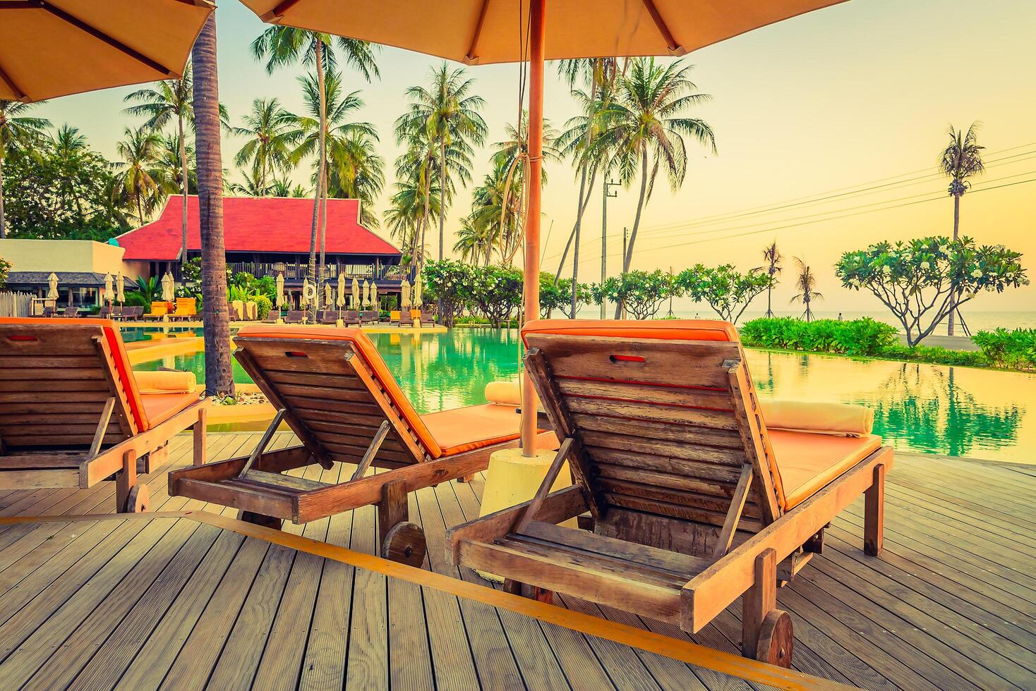 Two lounge chairs sit under an umbrella near a pool photo