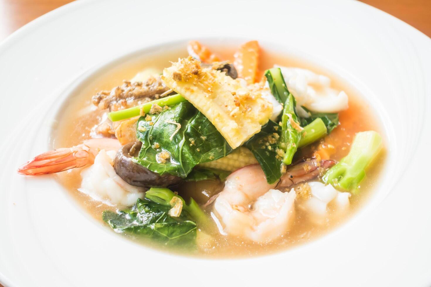 A bowl of soup with shrimp, vegetables and bread photo