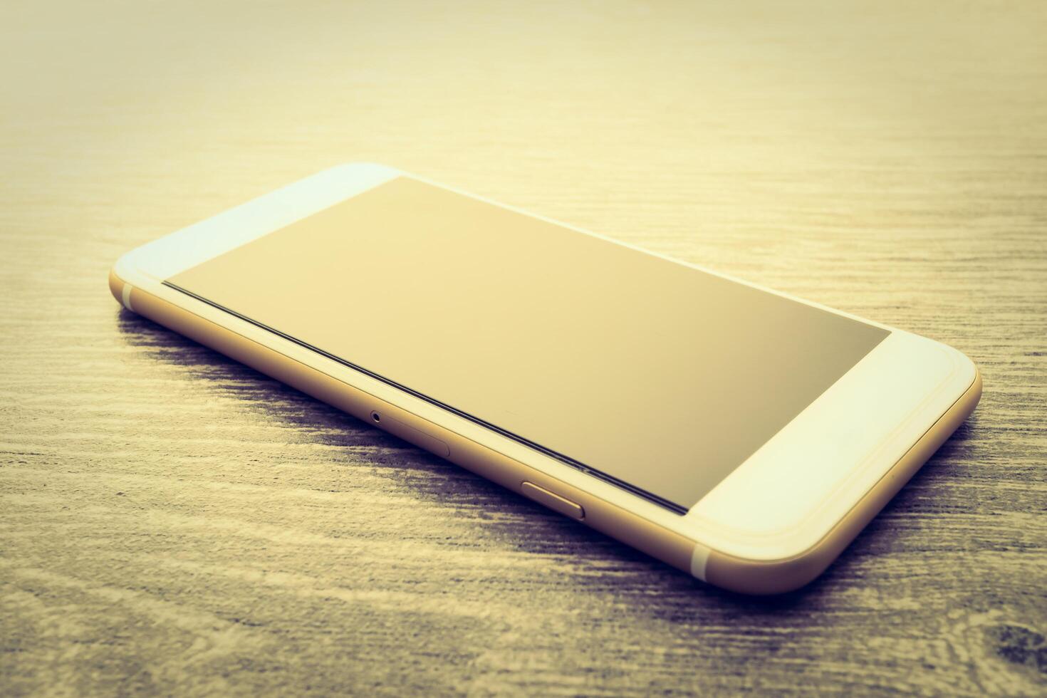 A white and gold cell phone sitting on a wooden table photo