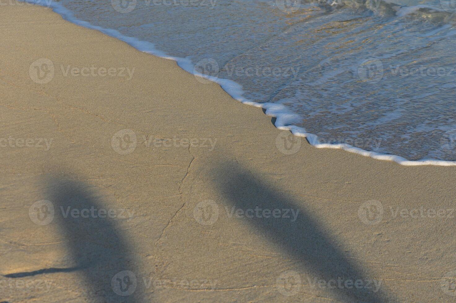 Two figures create shadows while frolicking by the shore as gentle waves lap against the sandy beach photo