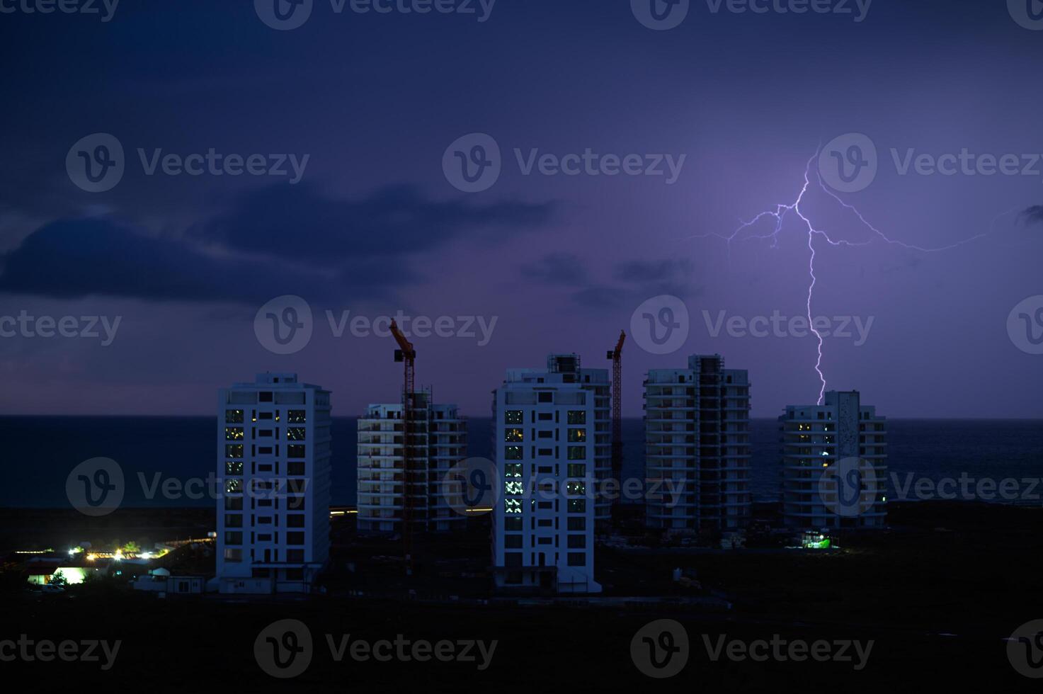 Lightning strikes over oceanfront construction at dusk in a vibrant coastal city skyline photo