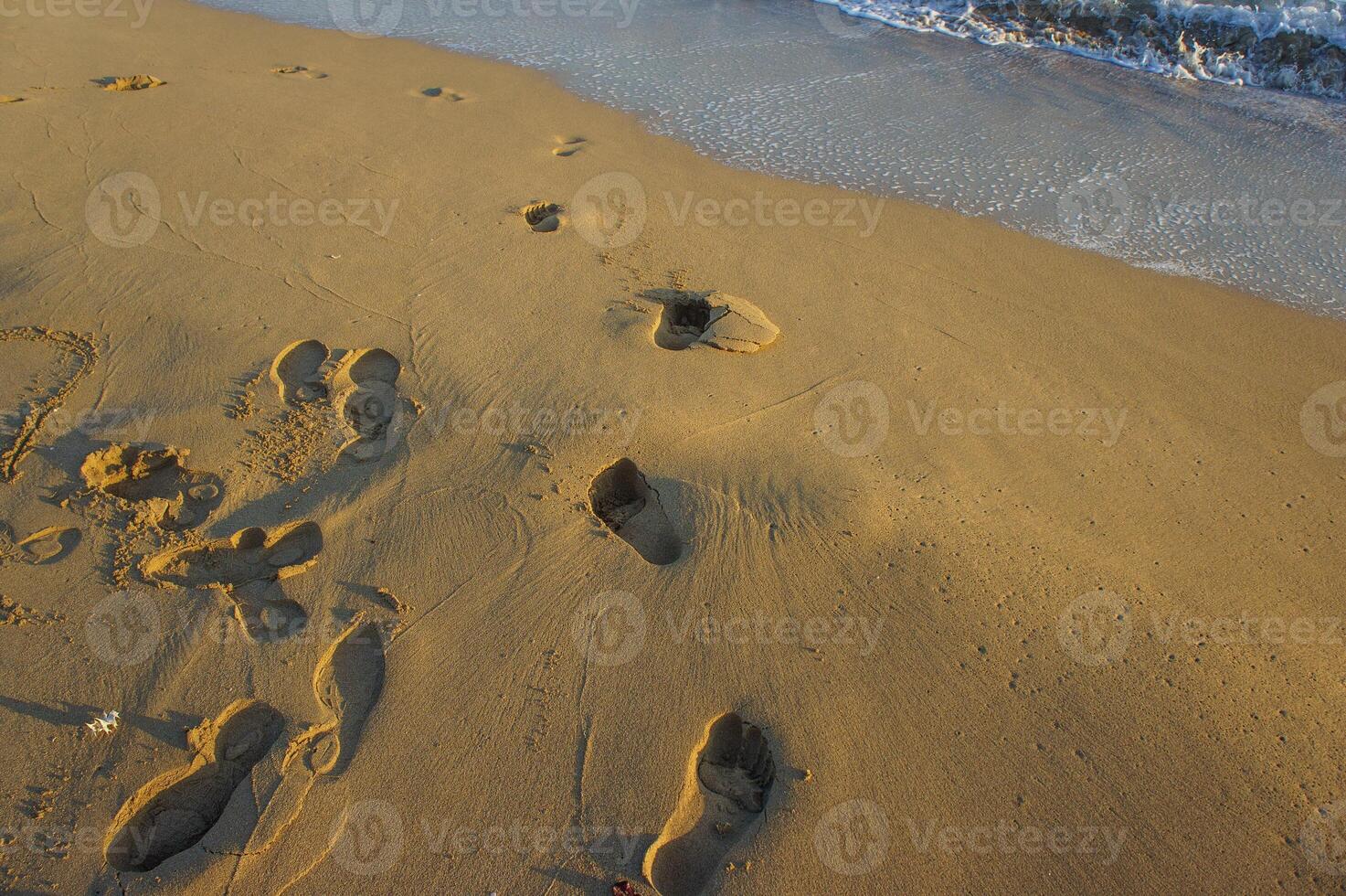 Footprints in the sand tell stories of wanderers at sunset by the serene ocean shoreline. photo