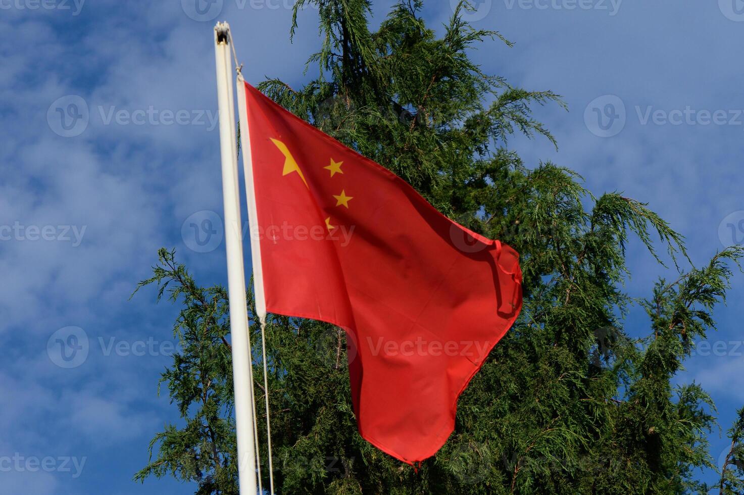 The Chinese flag waves gracefully against a backdrop of greenery and a bright blue sky photo