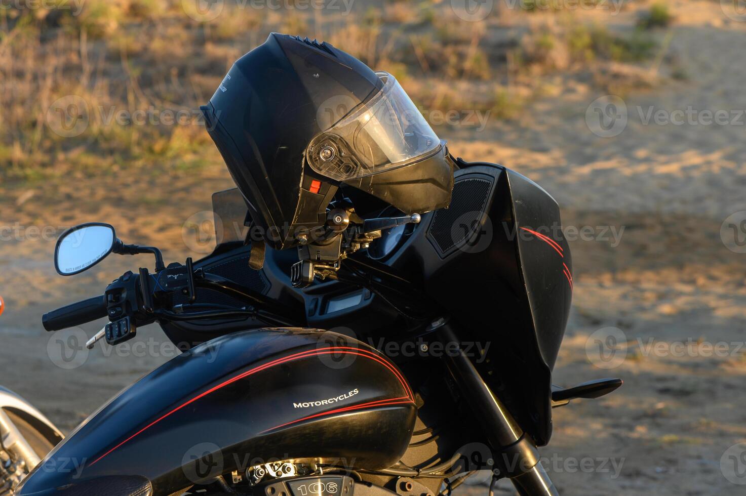 A sleek motorcycle parked on a sandy beach at sunset with a black helmet resting on the handlebars. photo