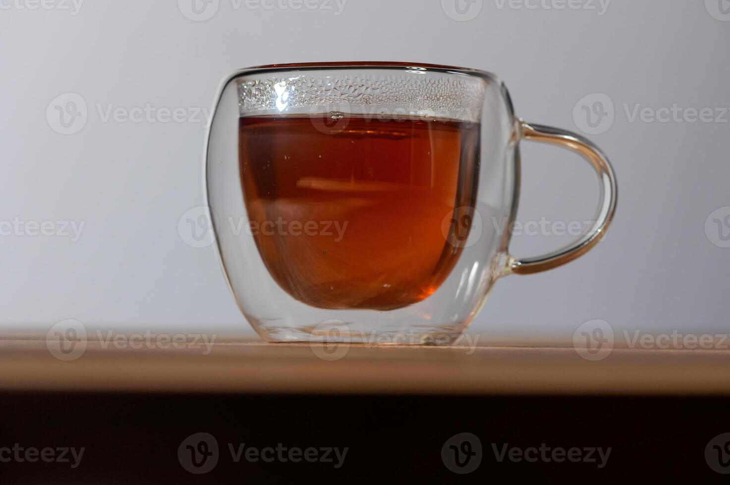 Warm embrace of tea in a clear glass cup resting on a wooden table during a peaceful afternoon photo