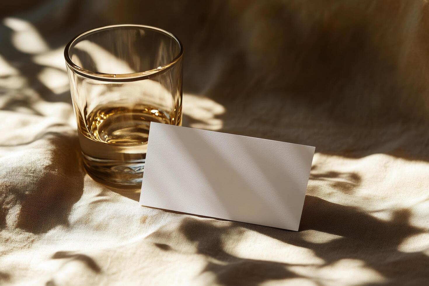 A clear glass with amber liquid next to a blank card on a softly lit table in a cozy setting photo