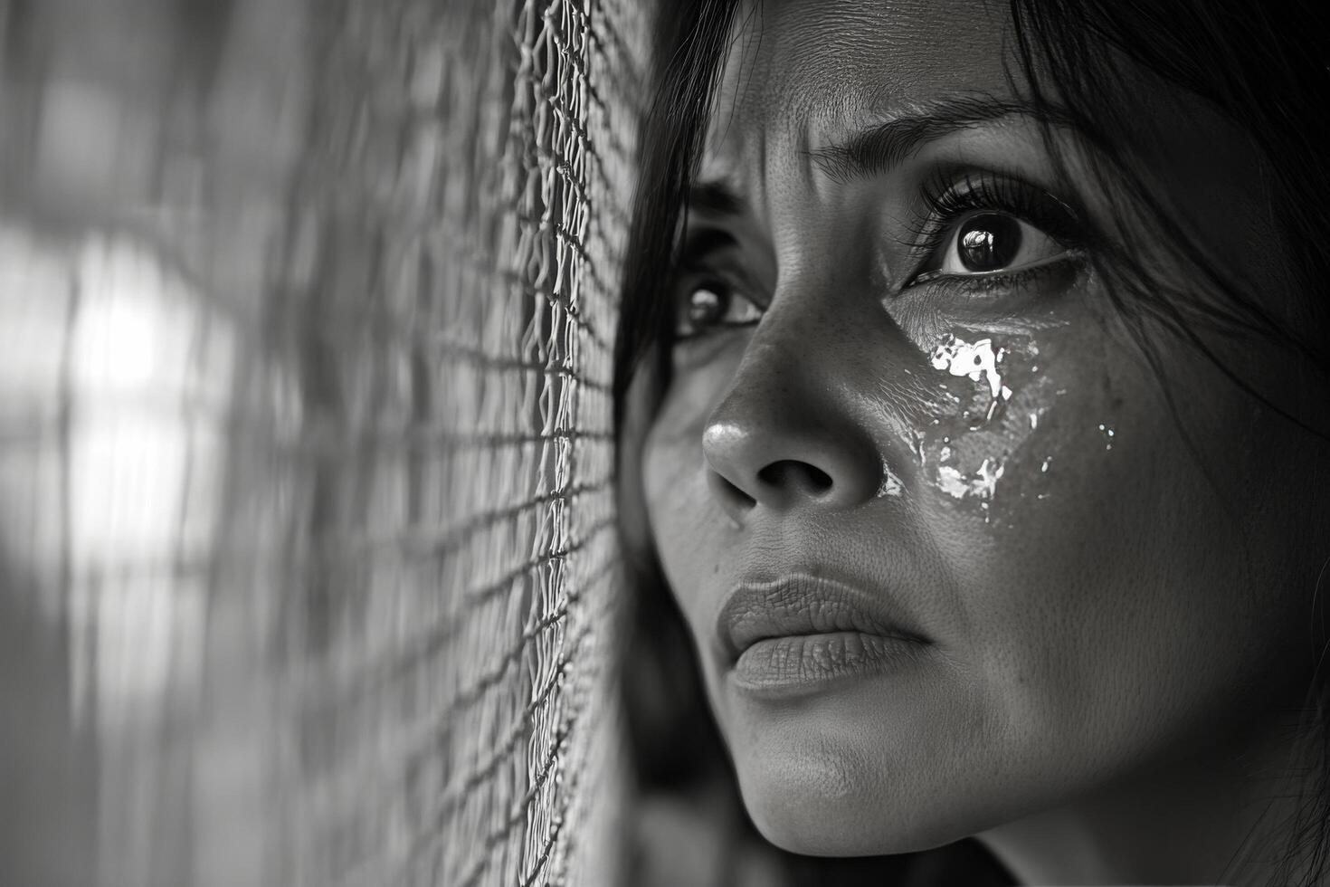 A close up of a distressed woman with tears streaming down her face amid a somber backdrop photo