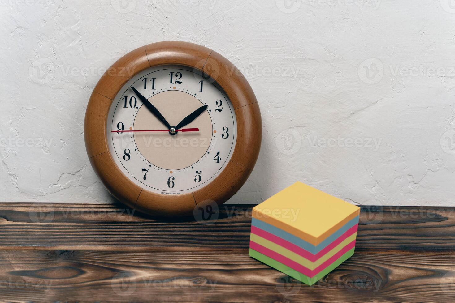 Wooden clock displays time next to colorful sticky notes on table photo