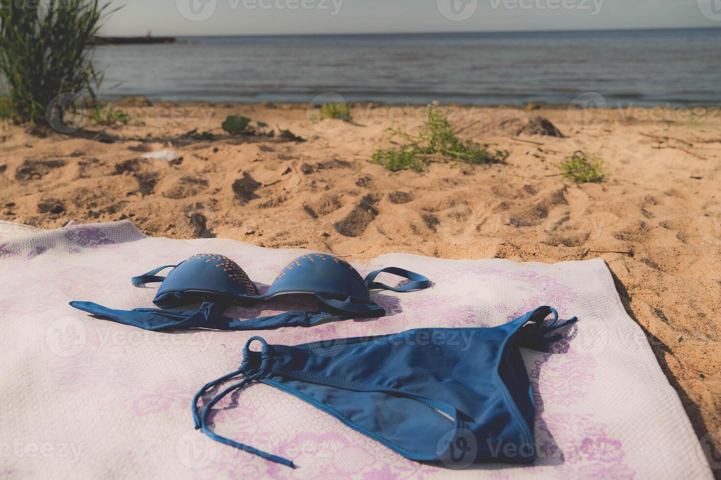 A blue bikini is laid on a sandy beach near the water photo