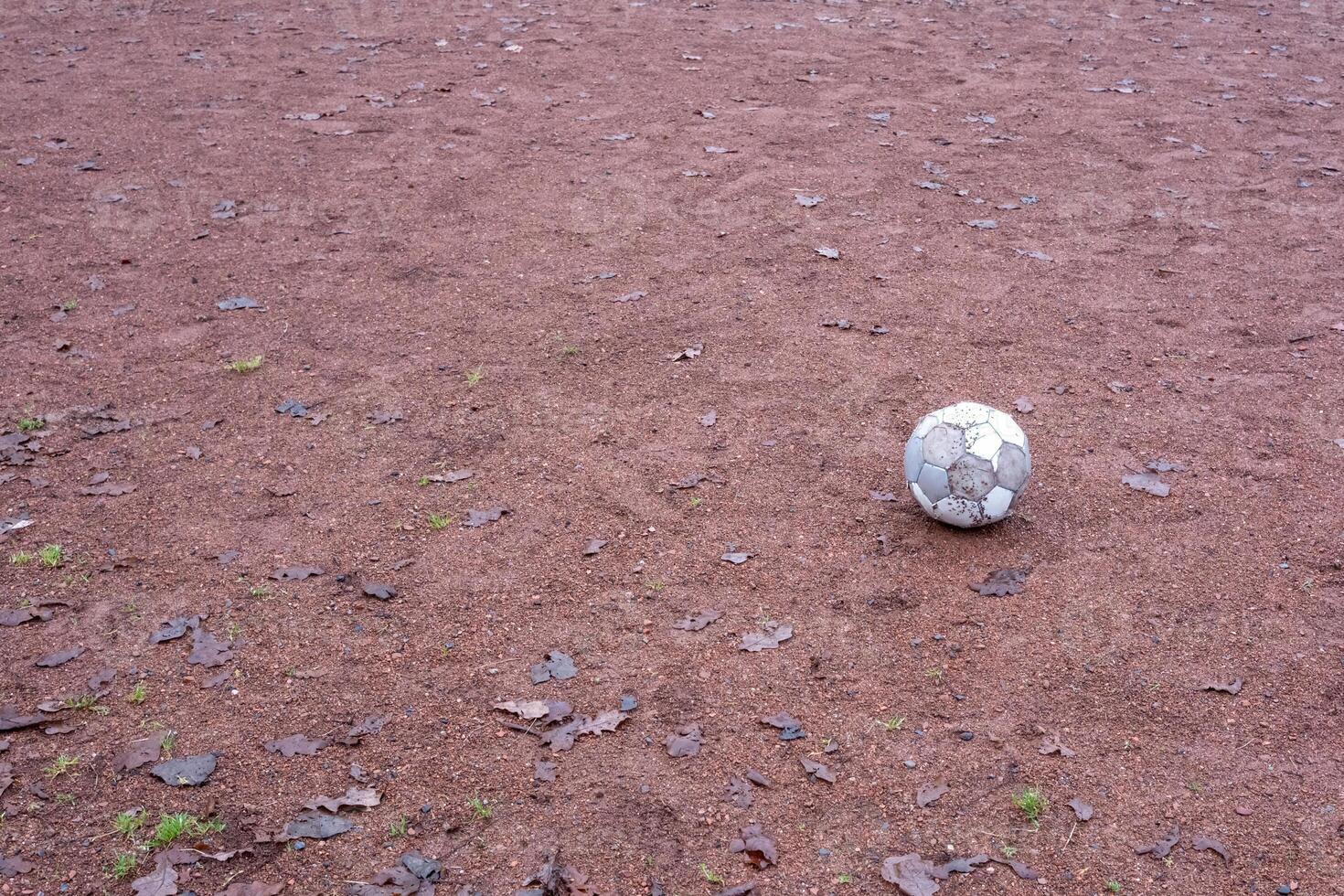 Old deflated soccer ball lying on a deserted gravel playground photo
