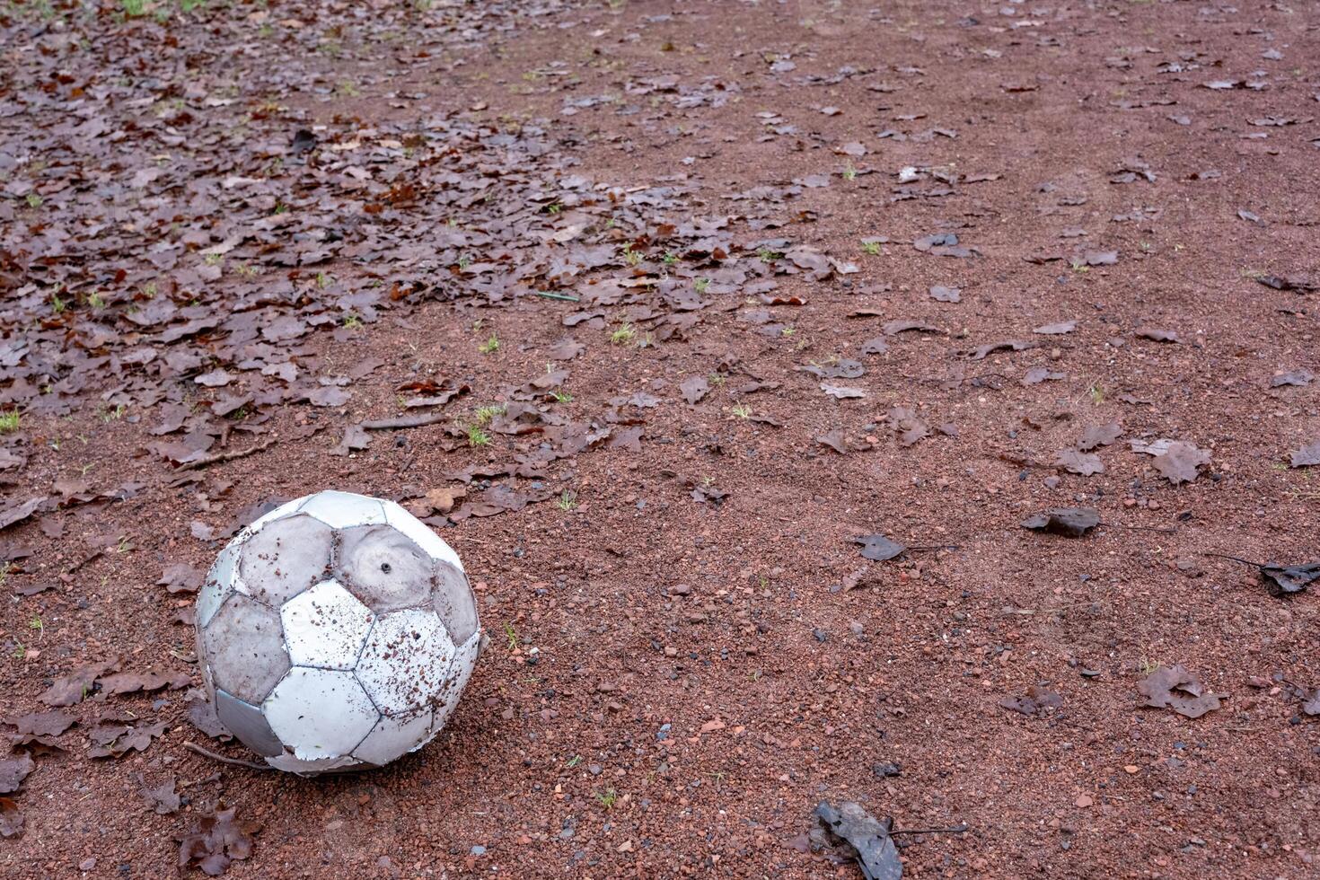 Old deflated soccer ball lying on a gravel field covered with dry leaves photo