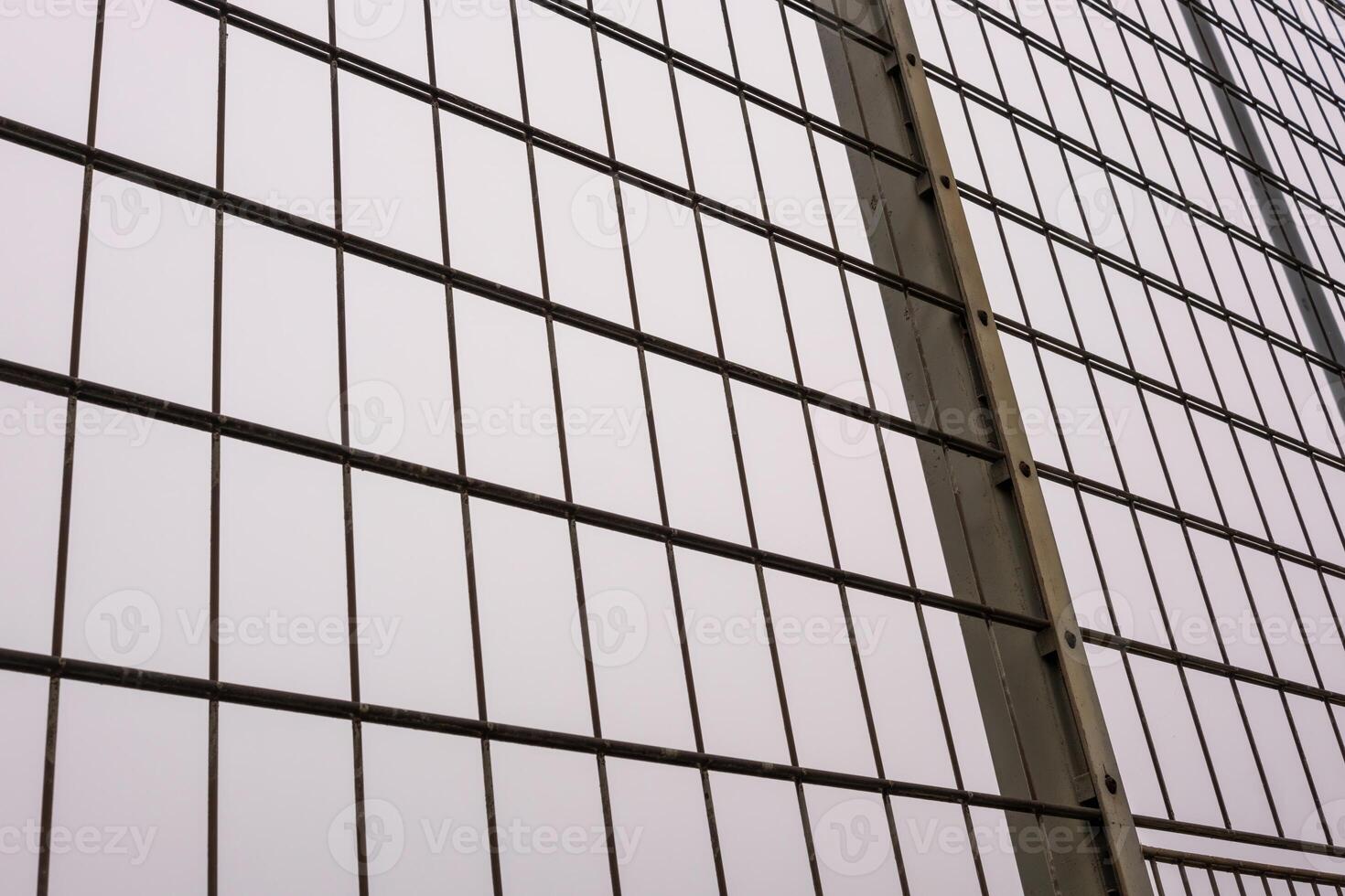 Metal mesh wire fence creating repeating pattern against cloudy sky photo