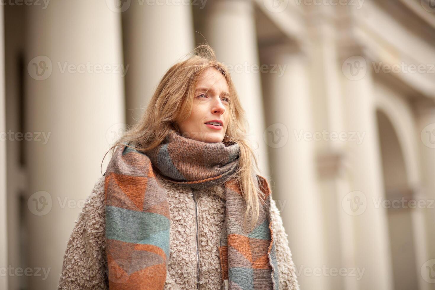 Woman in a cozy scarf walks near classical architecture on a sunny day photo