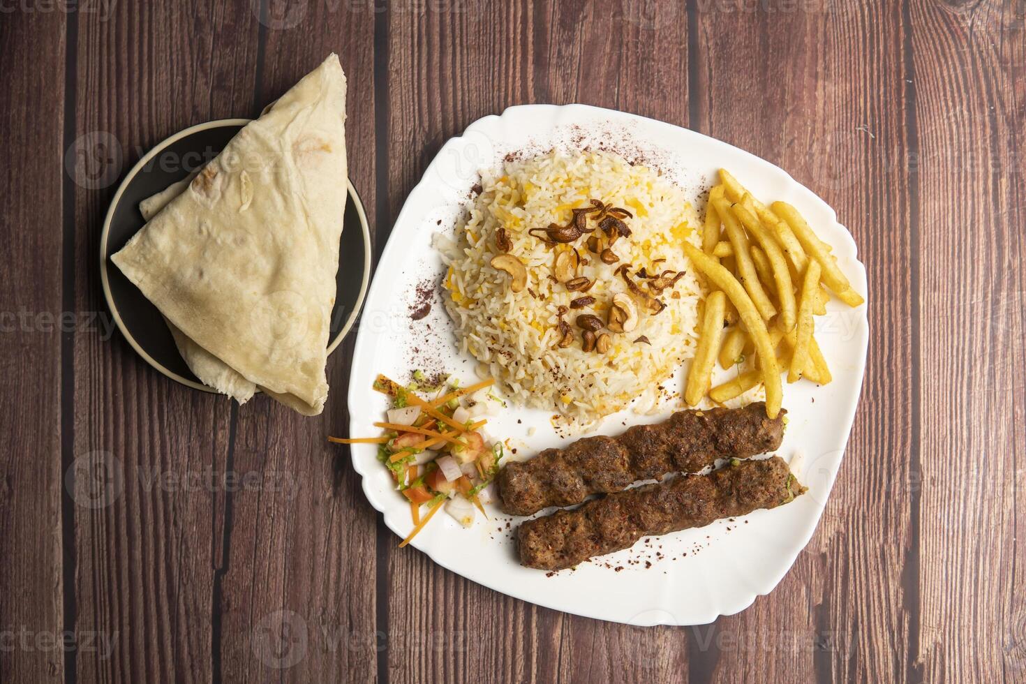 Beef Adana kebab with rice, french fries, salad and pita bread served in plate isolated on wooden table top view of turkish food photo