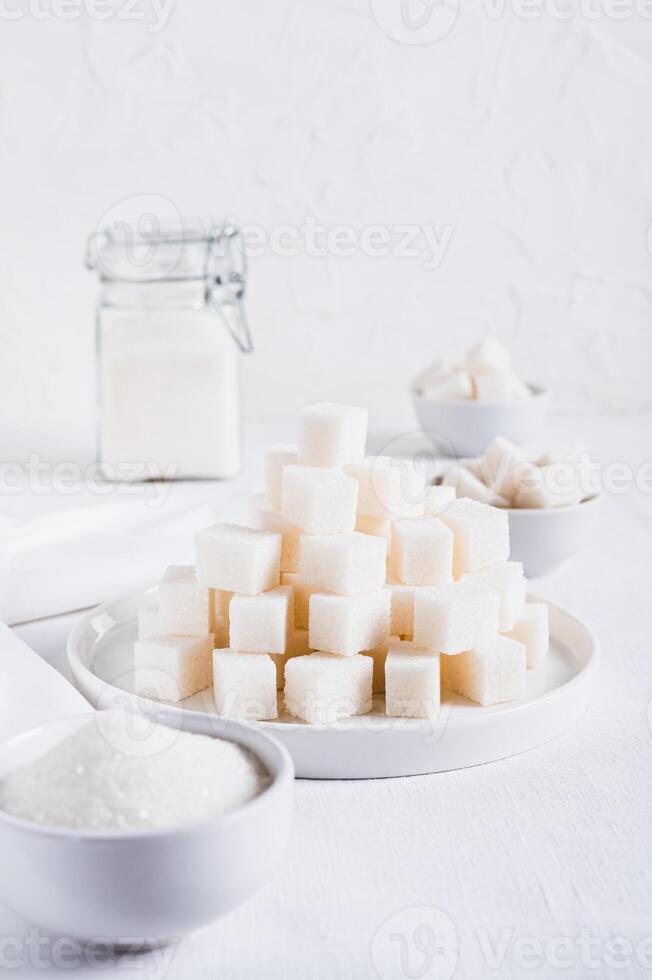 Lump sugar on a plate and granulated sugar in a bowl and jar on the table vertical view photo