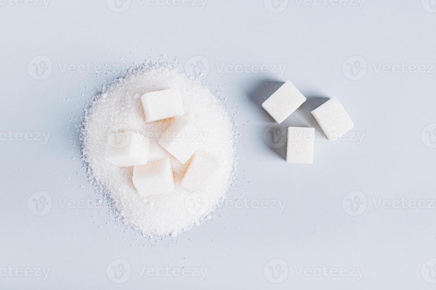 Lump sugar on a pile of granulated sugar and next to it on a blue background, top view photo