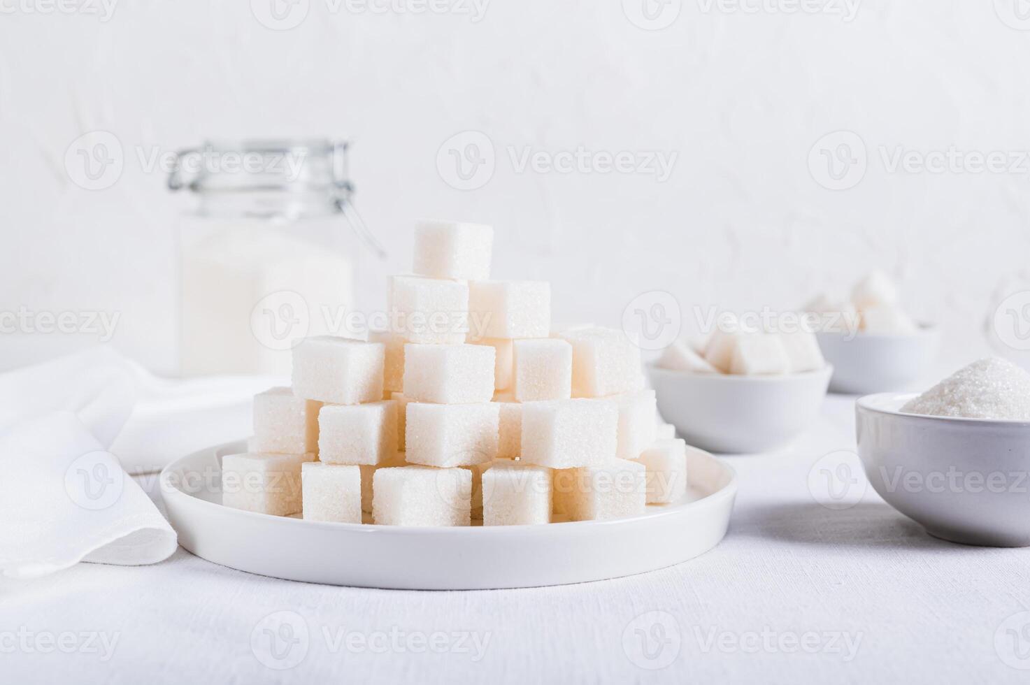 Lump sugar on a plate and granulated sugar in a bowl and jar on the table photo