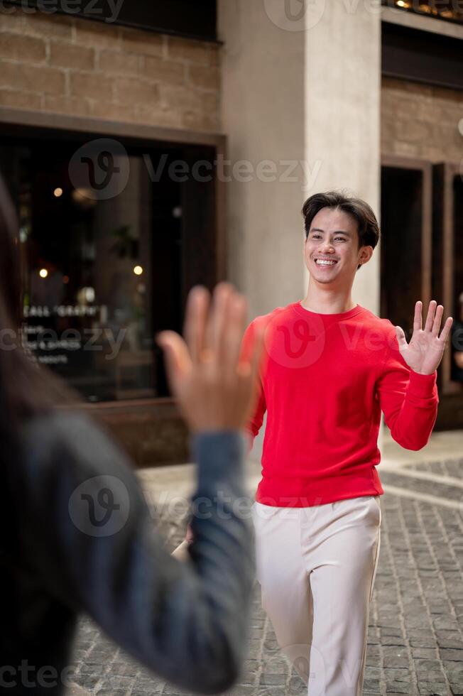 A happy Asian man is waving at his friend to say hi, after an unexpected meeting in the city. photo