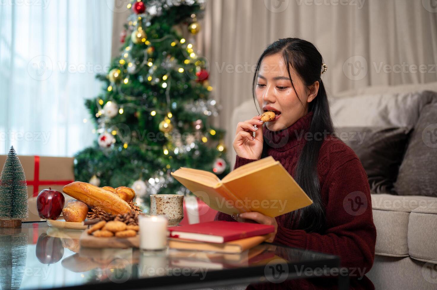 A beautiful Asian woman sits in her living room, reading a book during the Christmas holiday. photo